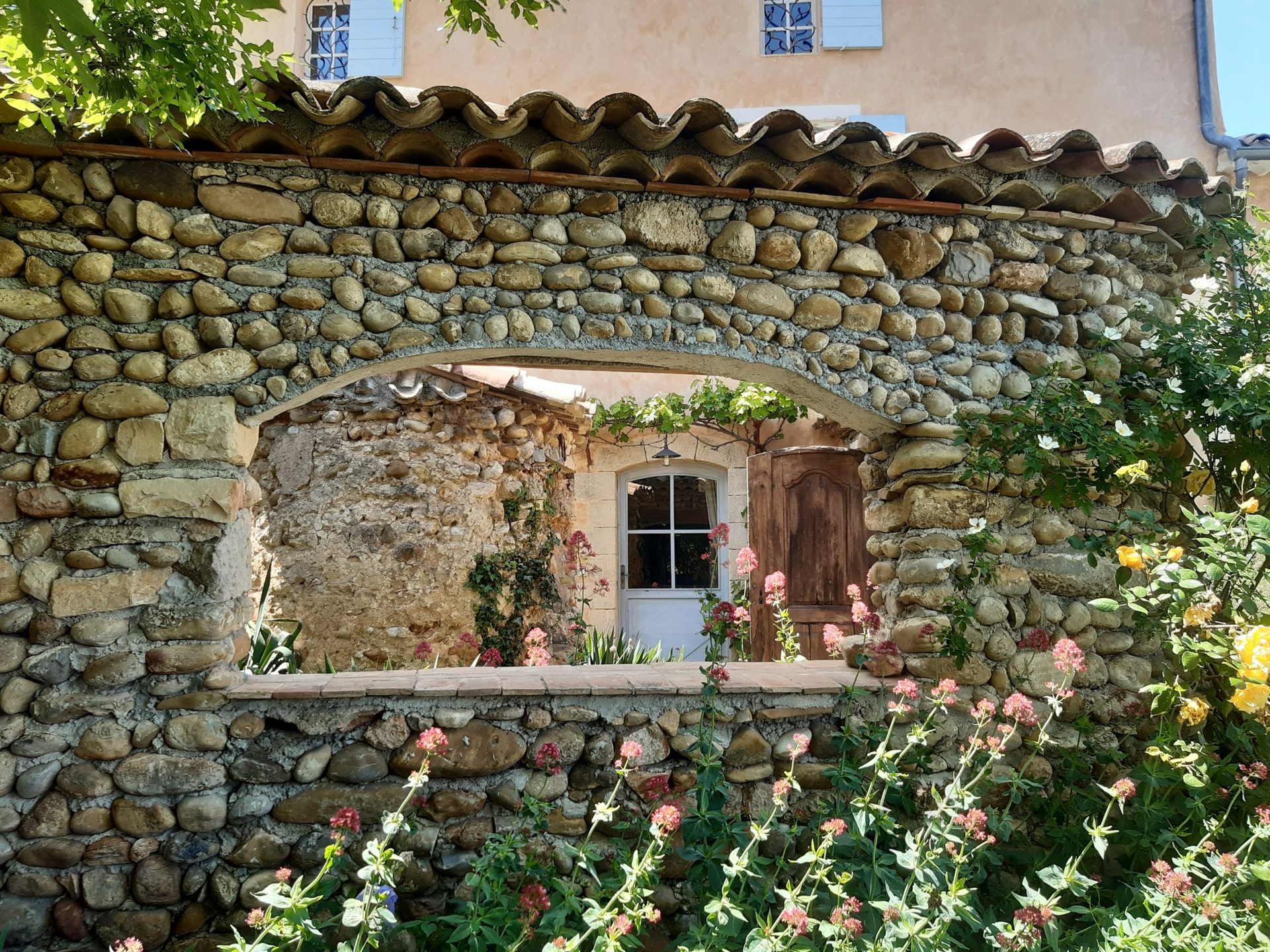 Arche dans un mur de galets, fleurs du jardin
