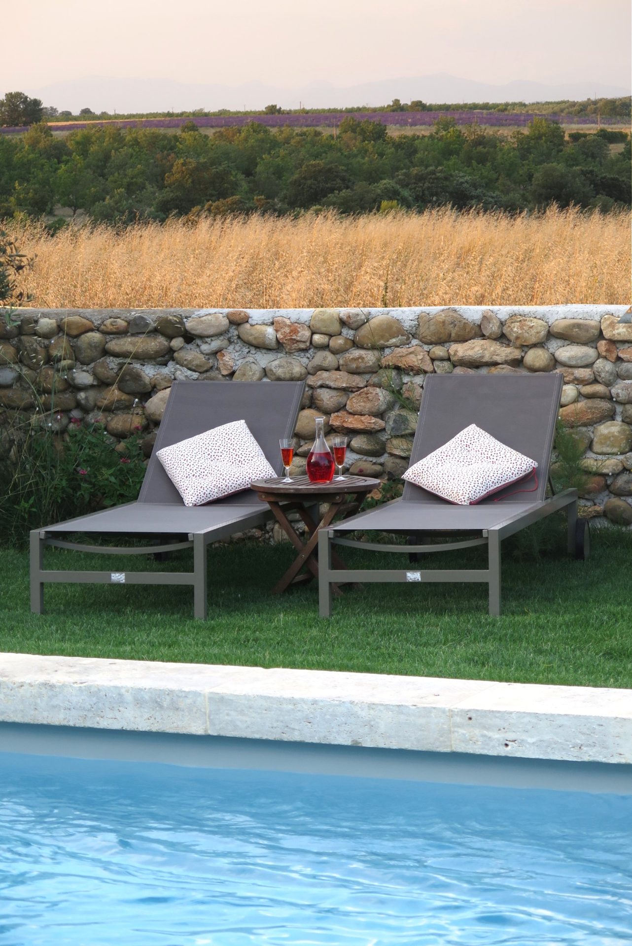 Deux transats au bord de la piscine, champ de blé et lavande derrière